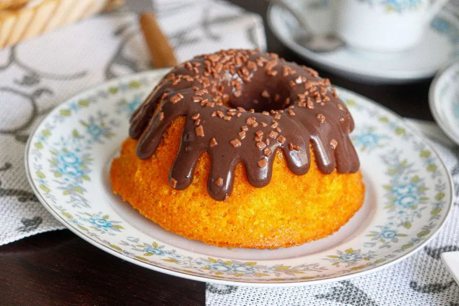 Brazilian carrot cake adorned with rich chocolate drizzle and sprinkles, served on a decorative plate.