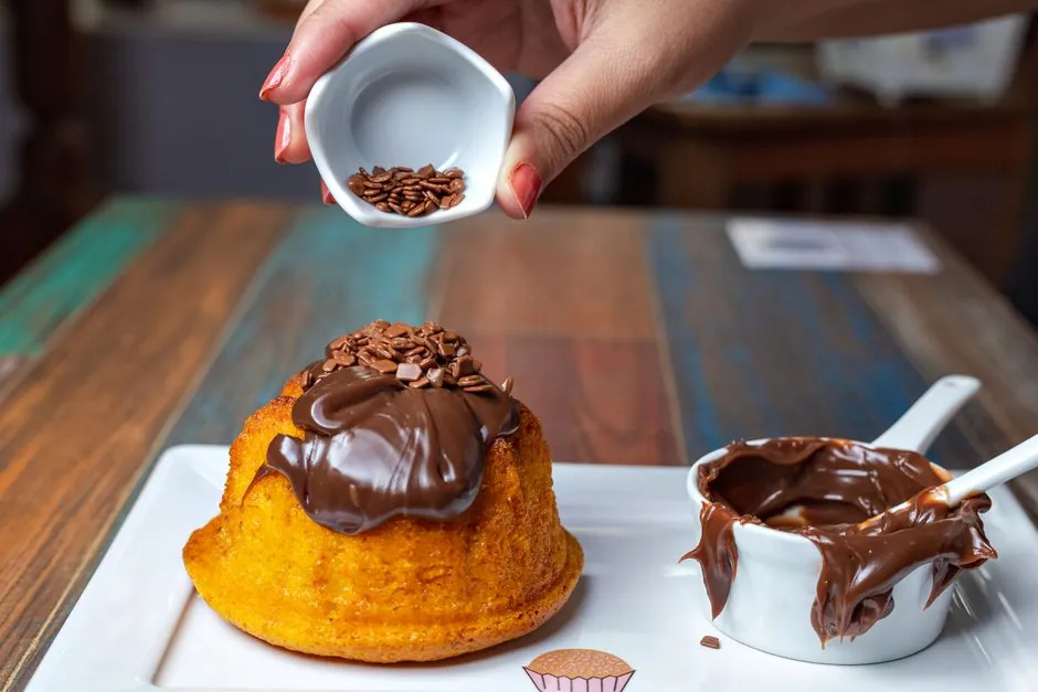 Close-up of a lava cake being topped with chocolate sprinkles and sauce, perfect for dessert lovers.