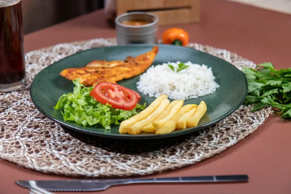 Appetizing meal featuring grilled fish, rice, and fries with fresh salad on a woven mat.
