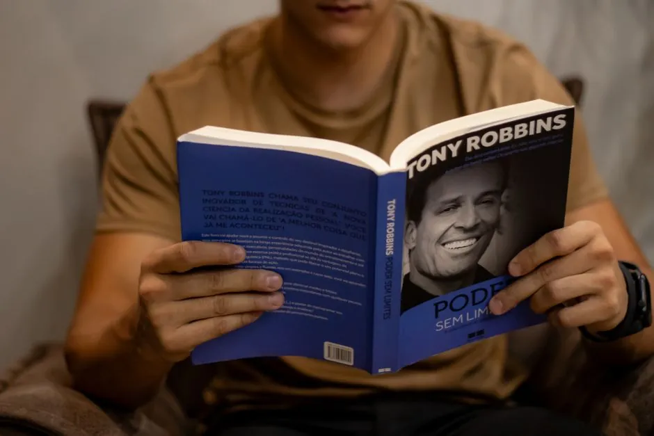 Close-up of a person reading 'Poder Sem Limites' by Tony Robbins indoors.