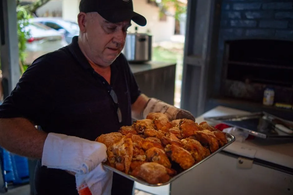 A man carrying a tray of roasted chicken in a rustic kitchen setting.