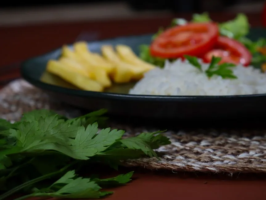 A vibrant meal featuring rice, fries, and fresh vegetables on a dark plate.