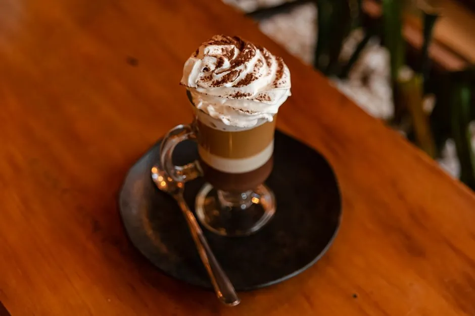 A close-up of a layered coffee topped with whipped cream served on a dark plate.