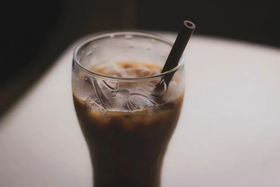 Close-up of an iced coffee with a straw on a table, emphasizing refreshment and taste.