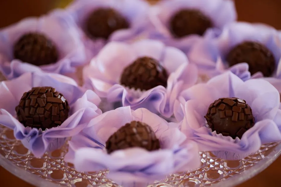 Chocolate brigadeiros beautifully presented in purple flower-like wrappers on a decorative tray.
