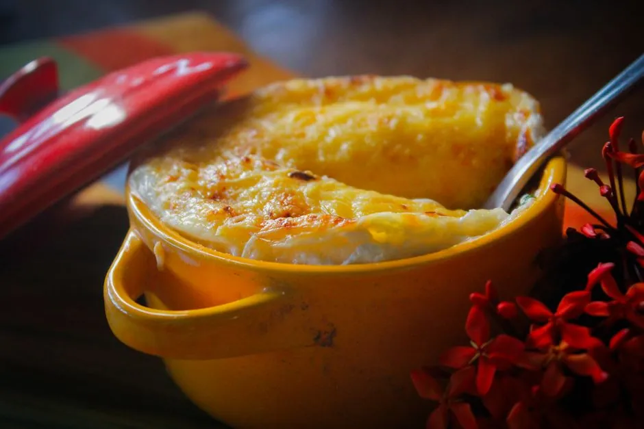 Savory dish topped with melted cheese, served in a yellow pot with a red lid.