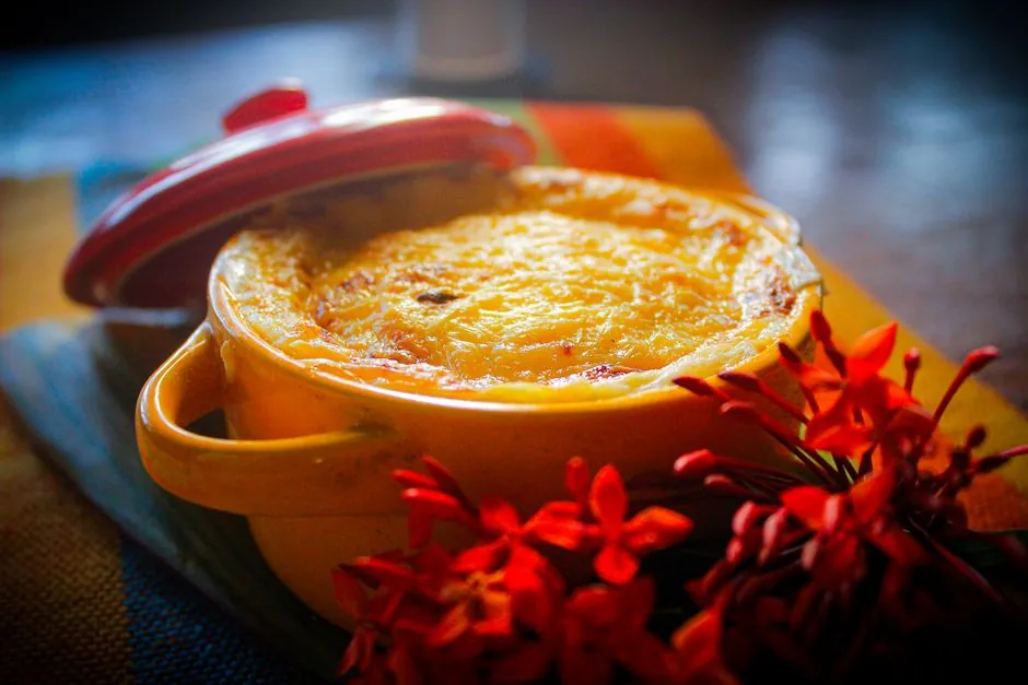 Warm baked dish in a yellow pot with vibrant red flowers on a colorful cloth.