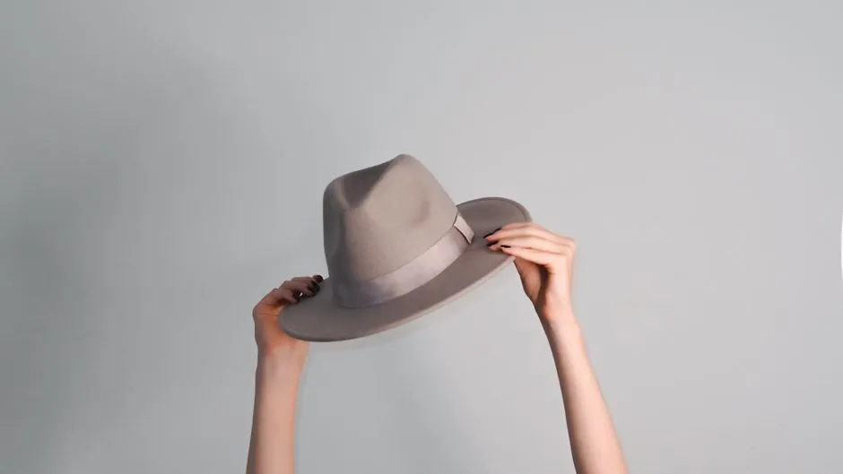 Stylish woman holding a gray hat on a minimalist backdrop. Fashion elegance in Paris.