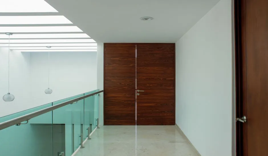 Stylish interior featuring a wooden door, glass railing, and ceiling lights in Pachuca de Soto, Mexico.