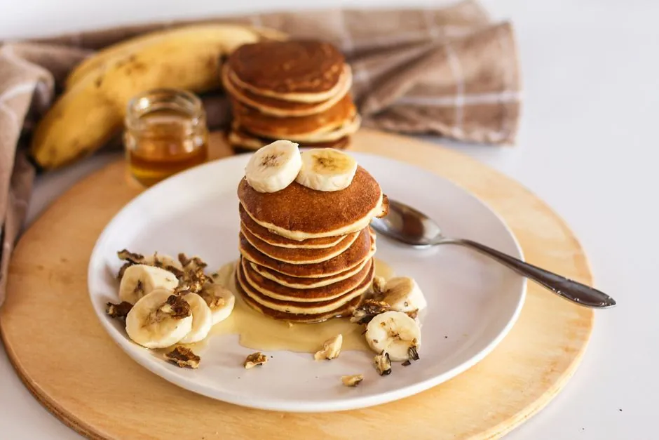 Stack of banana pancakes topped with honey and walnuts, served on a white plate.