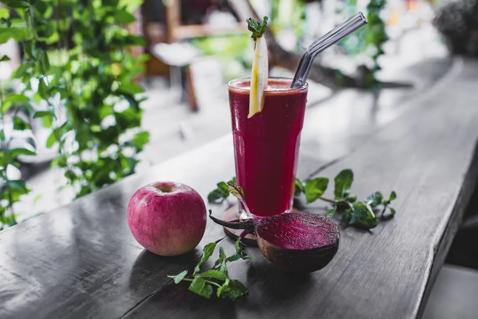 Glass of fresh cold healthy smoothie placed on wooden table on terrace of cafe with whole apple and halved beetroot