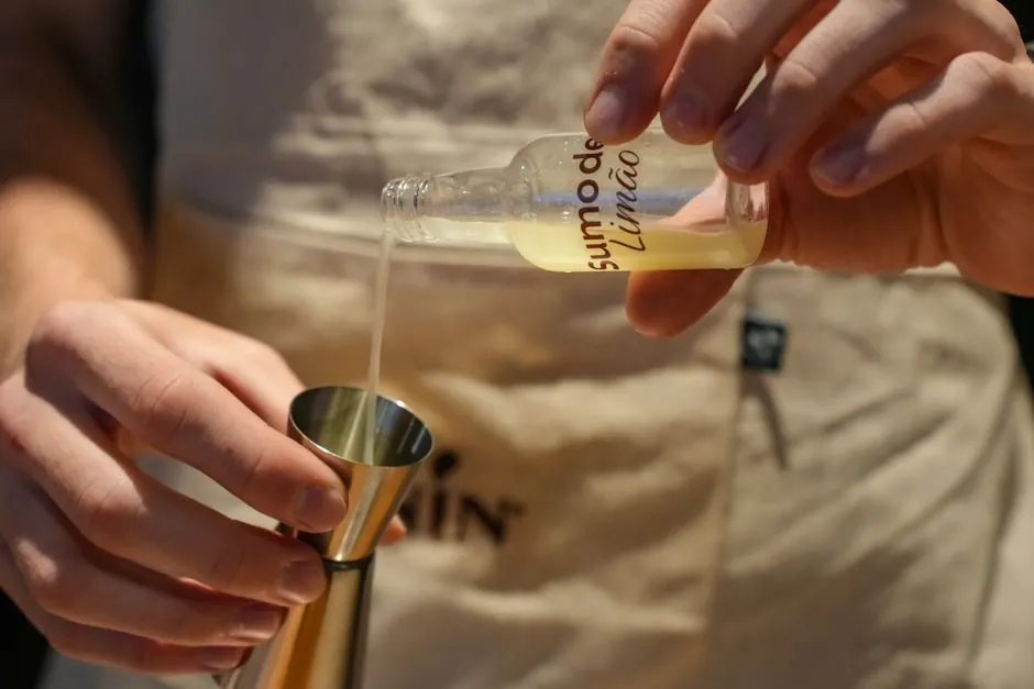 Close-up of bartender pouring lemon juice into a jigger for cocktail preparation.