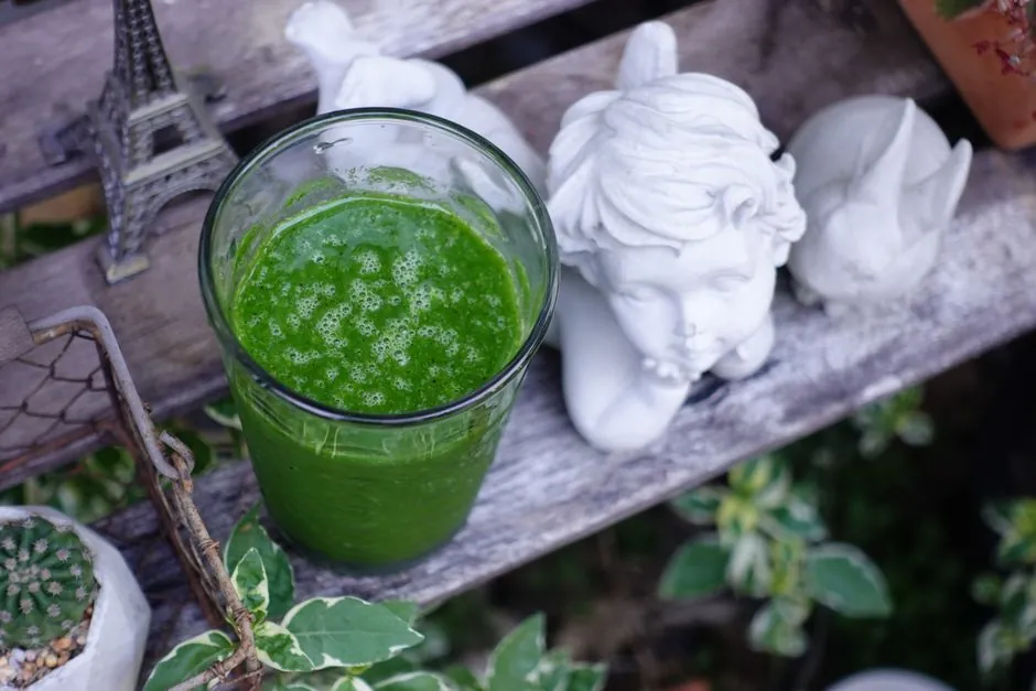 A vibrant green smoothie next to angel statue and Eiffel Tower model outdoors.