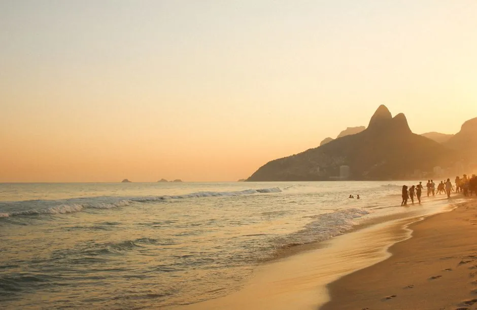 Breathtaking sunset view at Ipanema Beach, Rio de Janeiro with waves and mountains.