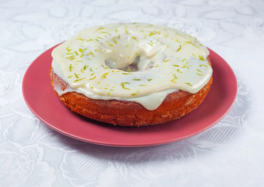 Close-up of a lime frosted bundt cake on a pink plate with intricate tablecloth.