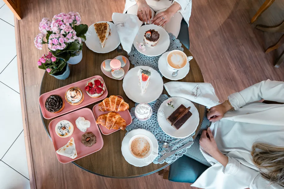 Overhead view of a stylish dessert table with pastries, cakes, coffee, and floral decor.