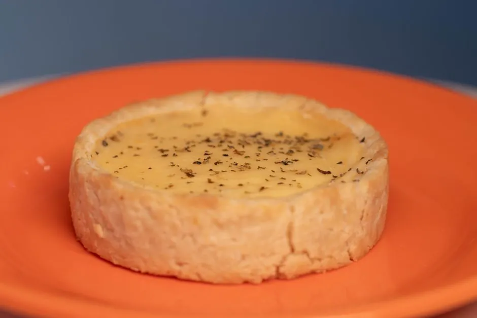Close-up of a delicious cheese tart garnished with herbs on an orange plate.