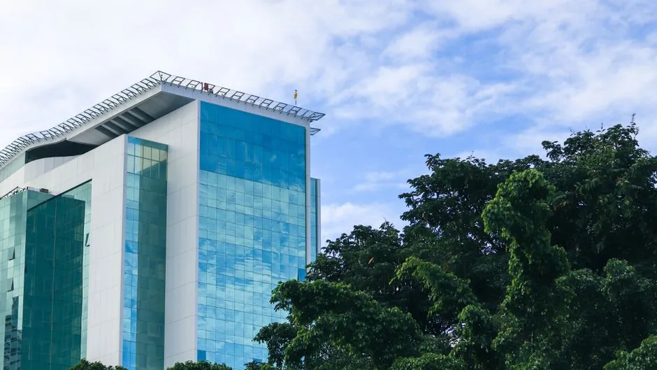 Sleek glass skyscraper in Ilha do Leite, Pernambuco, surrounded by trees and blue sky.