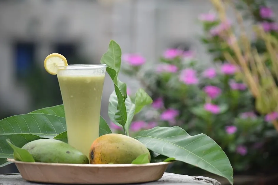 Chilled mango juice served with fresh mangoes and leaves, outside among flowers.
