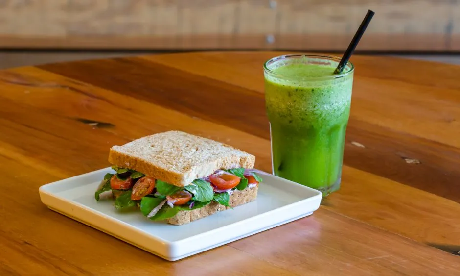 Colorful vegetable sandwich with a green smoothie on a wooden table.