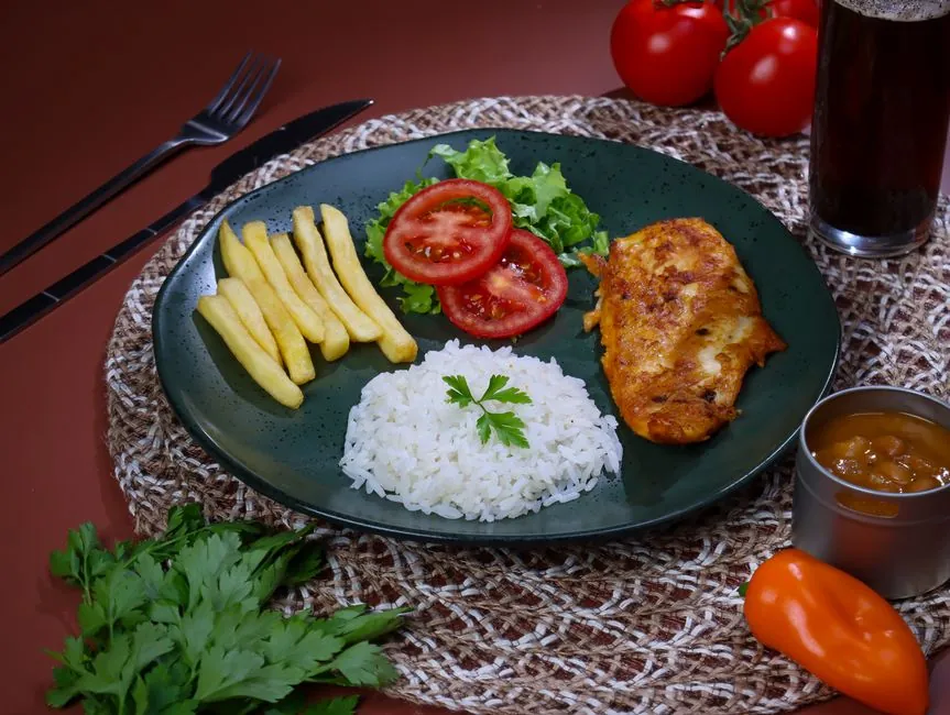 Appetizing dish featuring grilled chicken, fries, rice, tomato salad, ideal for food lovers.