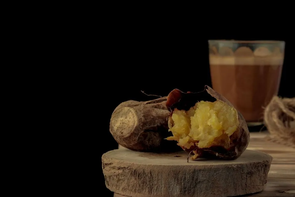 Still life of roasted sweet potato with a glass of coffee on a wooden table against a dark background.
