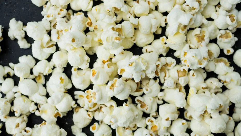 A close-up view of freshly popped popcorn scattered on a dark surface, ideal as a snack.
