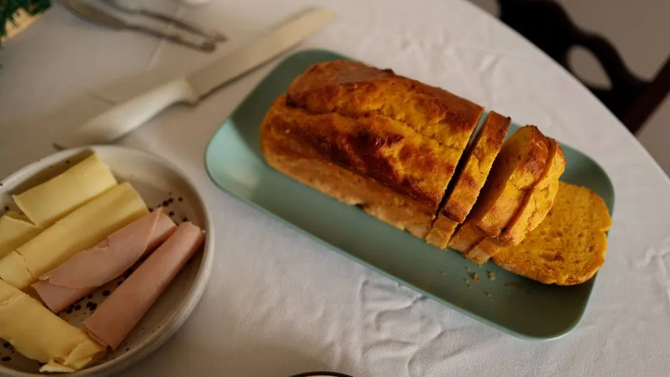 A detailed view of sliced pumpkin bread, cheese, and ham ready for breakfast on a white tablecloth.