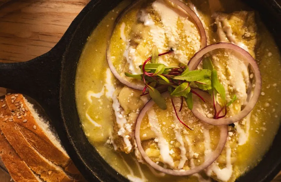 Close-up of Mexican Enchiladas Suizas garnished with red onion and cheese in a skillet.