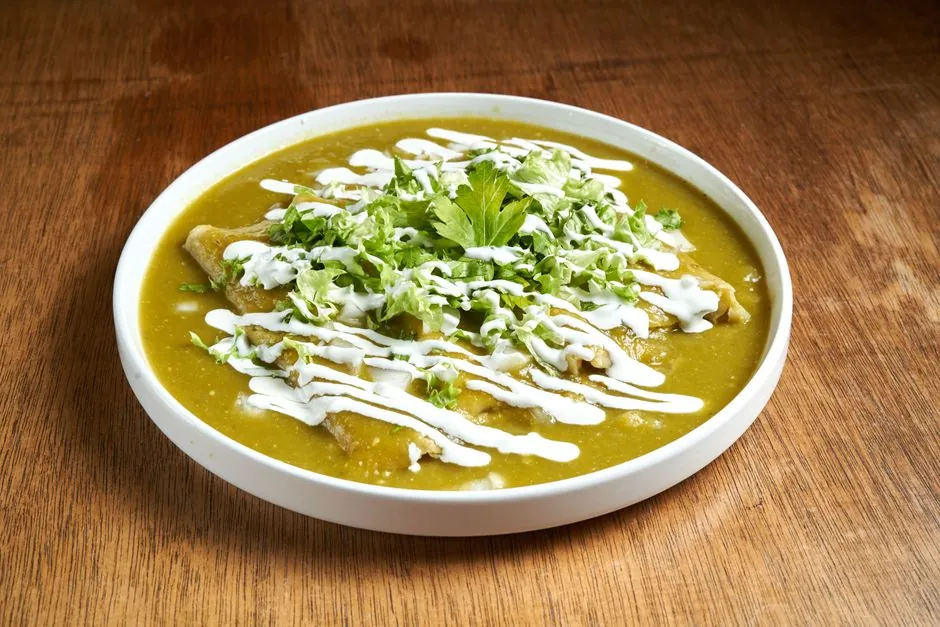 Plate of vibrant green enchiladas topped with fresh cilantro and creamy sauce.