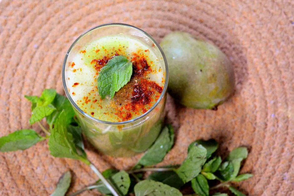 Top view of a refreshing glass of Aam Panna garnished with mint leaves and spices, placed on a woven mat.