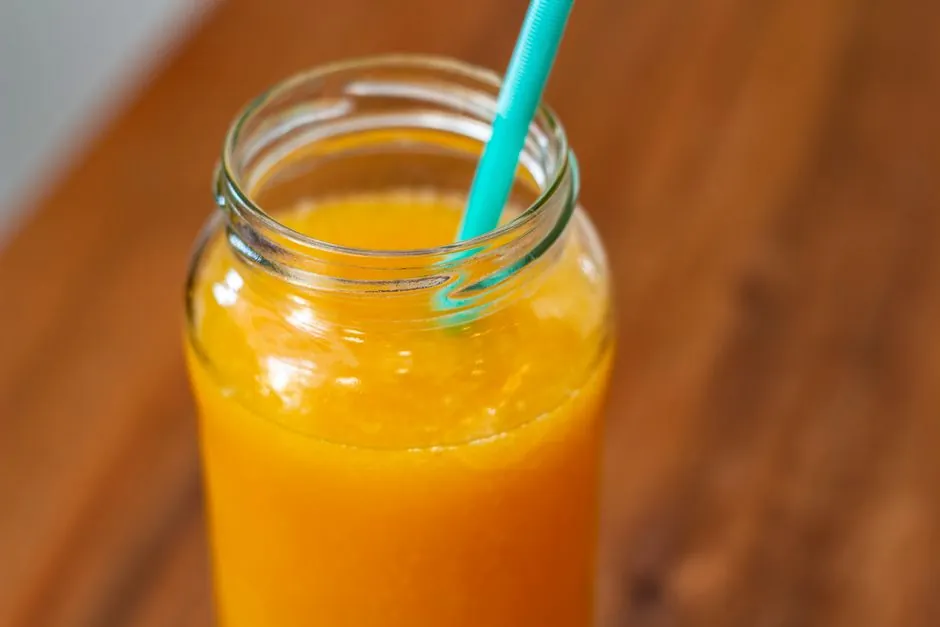 Close-up of fresh orange juice in a mason jar with teal straw on wooden table.