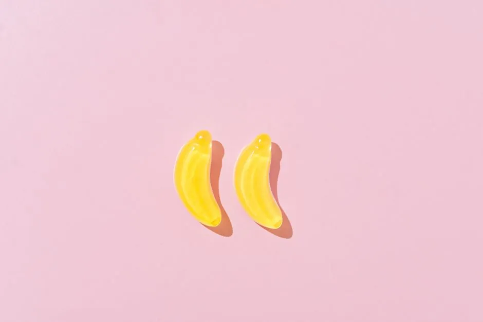 Bright yellow banana shaped candies on a pastel pink surface, perfect for sweet-themed designs.