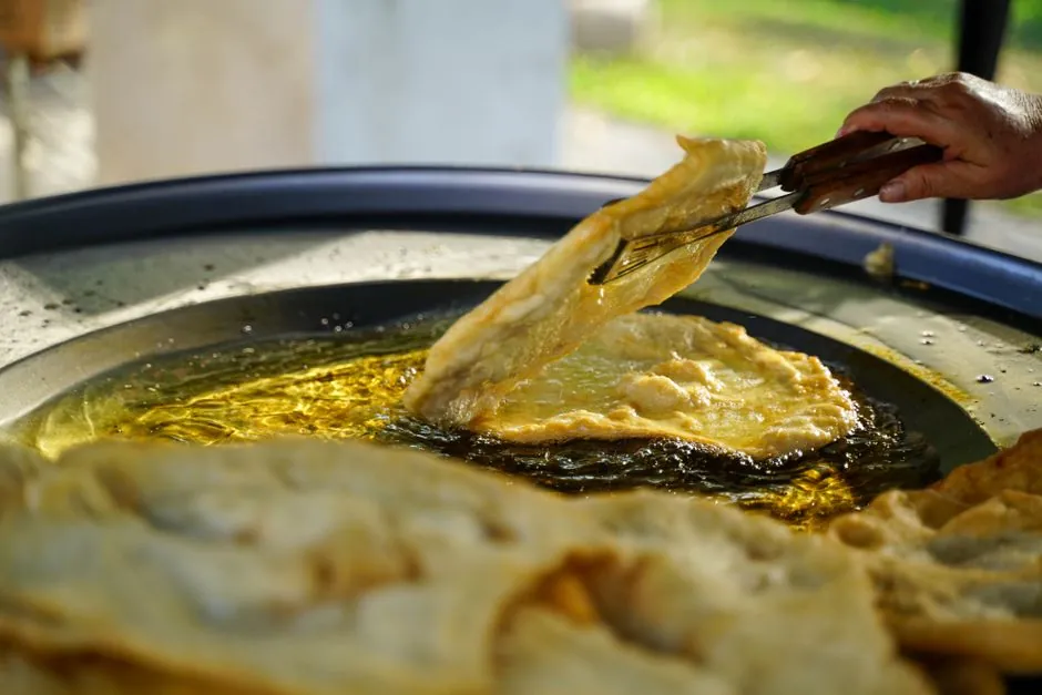 Close-up of hand frying traditional Croatian flatbread outdoors in olive oil.
