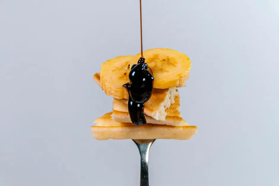 Close-up of banana slices on pancake with chocolate syrup on a fork. Minimalist, appetizing shot.