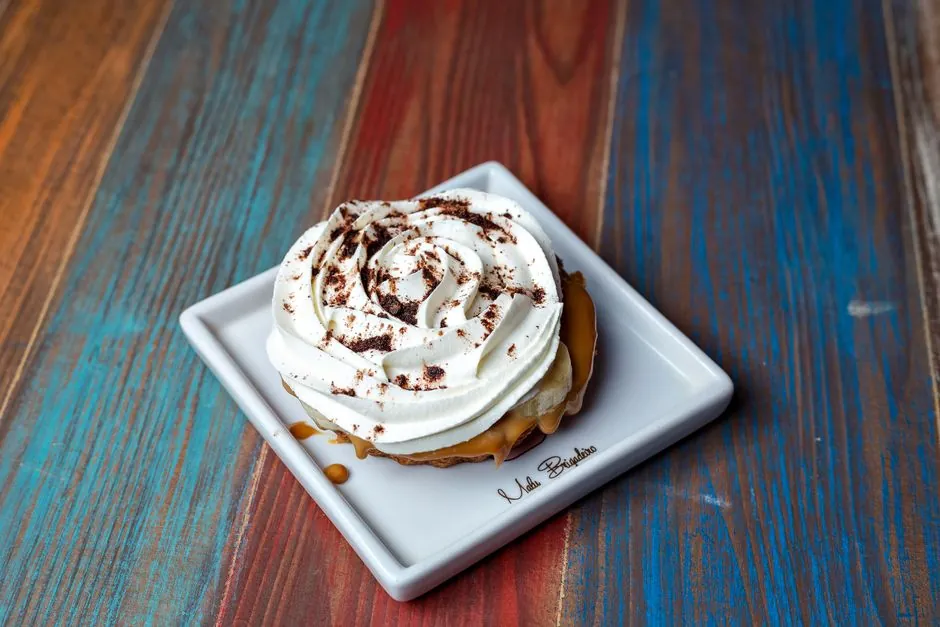 Close-up of a creamy banoffee pie with caramel and frosting on a ceramic plate.