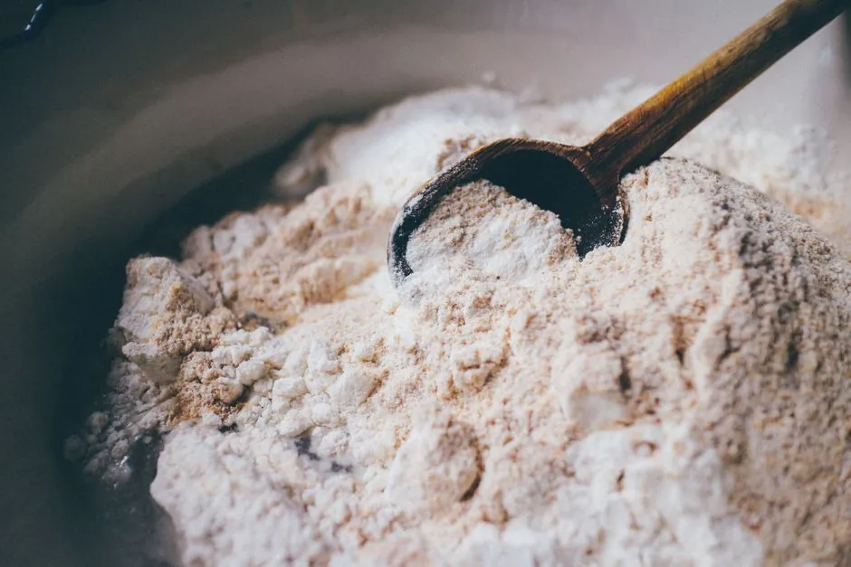 A close-up view of a wooden spoon resting in a mound of flour, perfect for baking themes.
