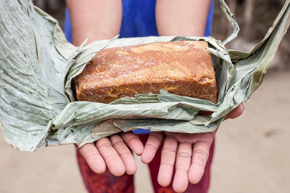 Close-up of traditional Colombian food wrapped in banana leaves held in hands.