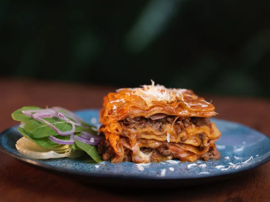 Close-up of a delicious homemade lasagna served with fresh salad on a ceramic plate.