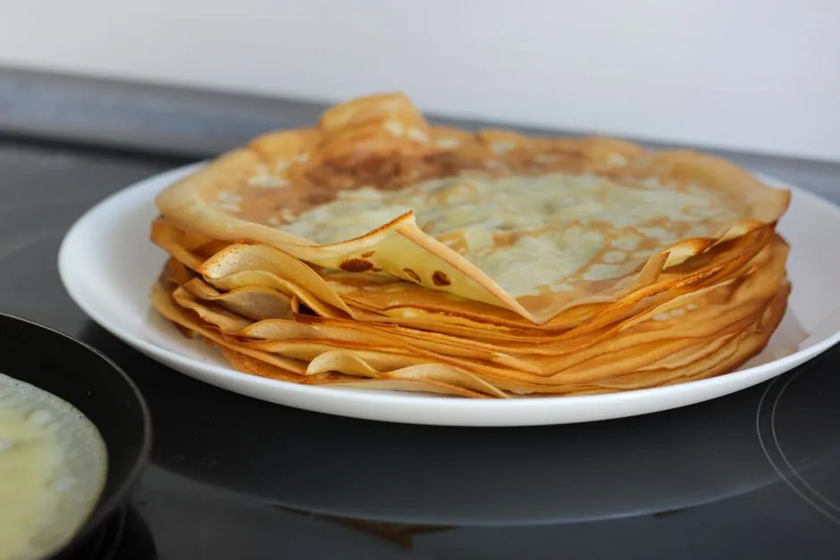 A delicious stack of golden-brown crepes on a white plate, perfect for breakfast or dessert.