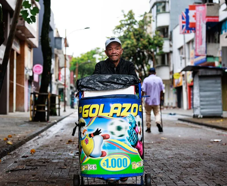 Street vendor in Pereira pushes colorful ice cream cart, lively urban scene.