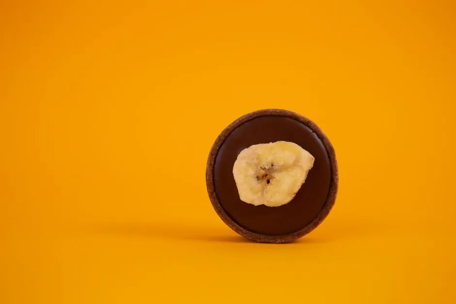 A minimalistic shot of a chocolate tart topped with banana slice on a bold yellow background.