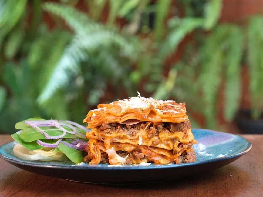 Close-up of layered lasagna with side salad on rustic plate.