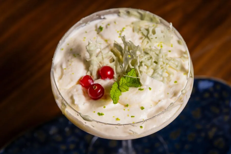 Elegant creamy dessert topped with fresh red berries and mint in a cocktail glass.