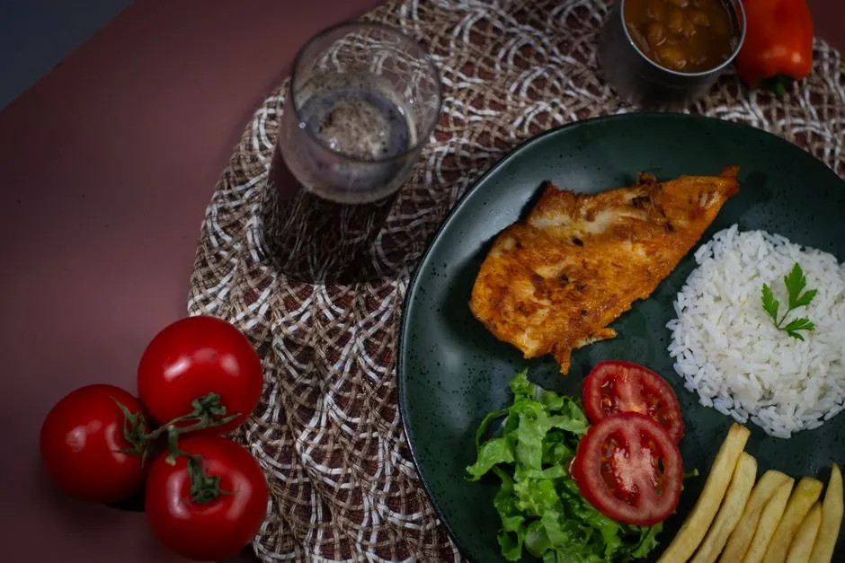 A vibrant plate featuring grilled chicken, rice, salad, and tomatoes, perfect for a healthy meal.