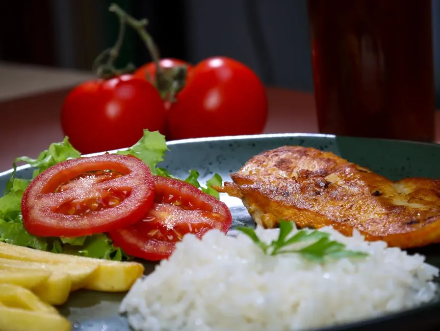 A vibrant plate with grilled chicken, rice, lettuce, tomatoes, and fries.