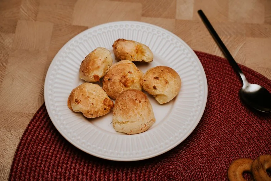 Plate of traditional Brazilian cheese bread rolls on a red mat with a spoon.