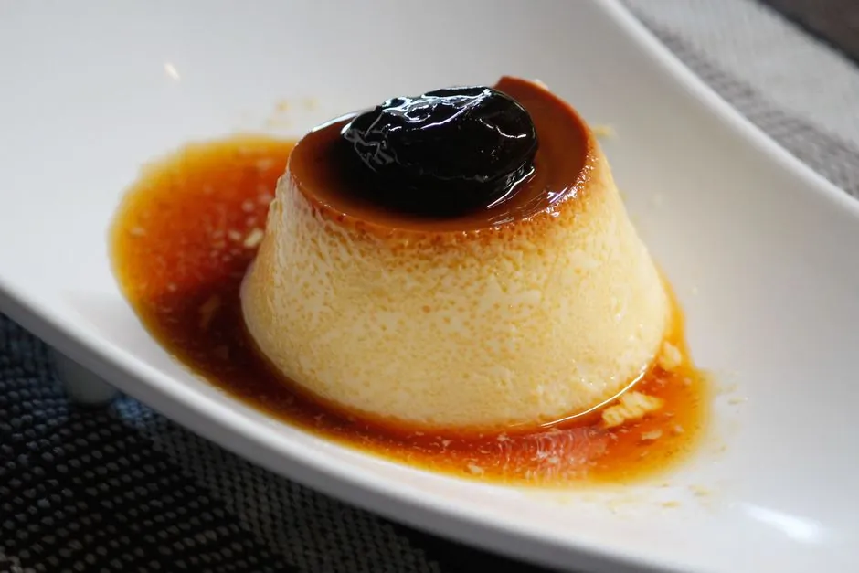 Appetizing caramel flan dessert with a rich prune topping served in a white dish.