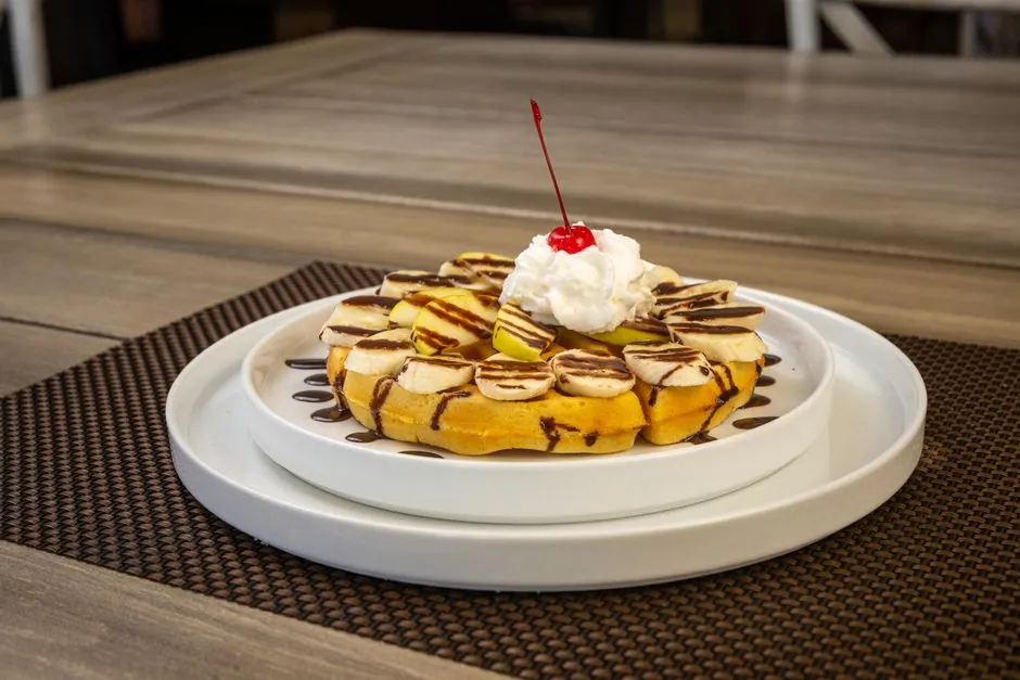 Scrumptious banana waffle topped with whipped cream, cherry, and chocolate drizzle. Perfect dessert shot.