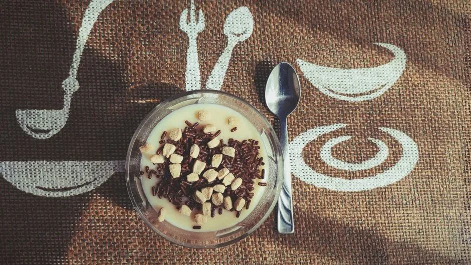 A tasty vanilla pudding topped with chocolate sprinkles and nuts, placed on a decorative mat.